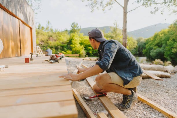 Photo of a carpenter working on wooden decking in front of the cabin house